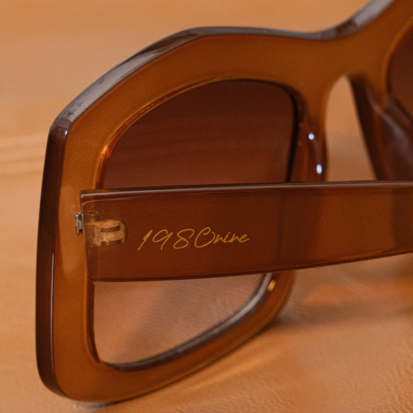 Brown sunglasses with '1980s' text on a brown leather surface