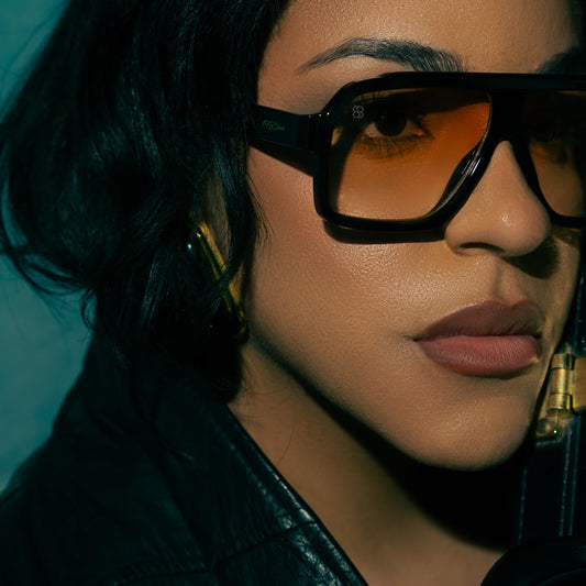 Model wearing oversized square sunglasses with thick black frame and warm amber lenses