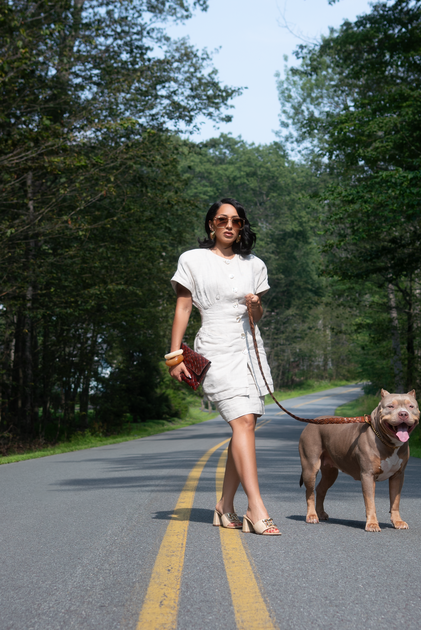Woman in a white dress walking a dog on a road surrounded by trees wearing timeless 1980nine sunglasses in Avion shade sheer-cream