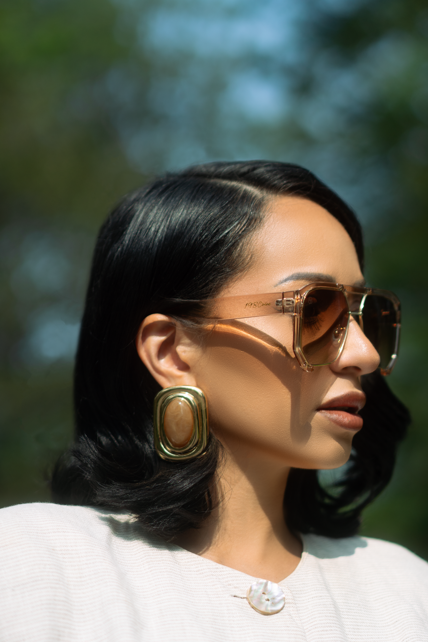 Woman wearing sunglasses with a blurred natural background wearing AVION sunglasses from 1980nine in shade sheer-cream.