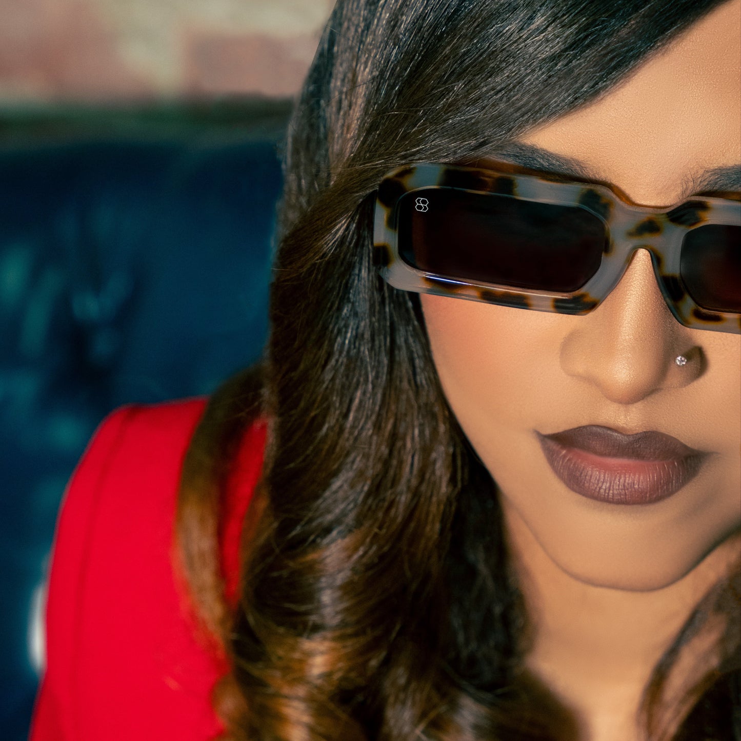 Person wearing sunglasses with a red garment and brick wall background