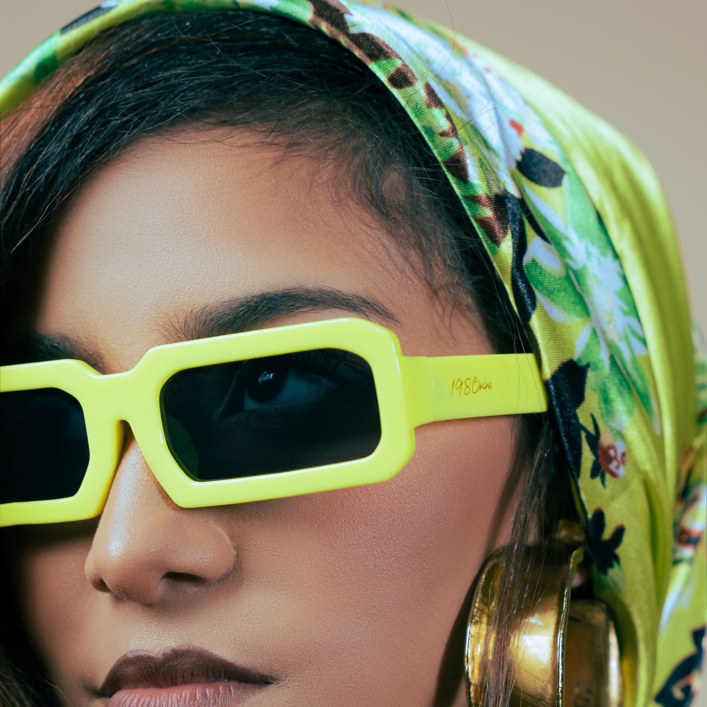 Person wearing a colorful headscarf and bright yellow sunglasses with a blurred background