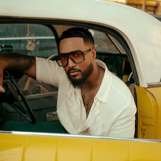 Man sitting in a yellow car wearing 1980nine oversized retro sunglasses and a white shirt.