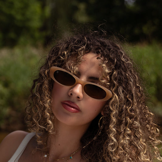 Woman with curly hair wearing sunglasses and a white top outdoors