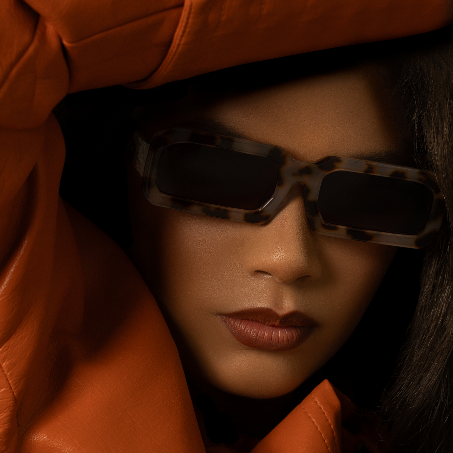 Person wearing tortoiseshell sunglasses and an orange leather jacket.