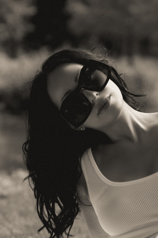 Black and white photo of a woman wearing sunglasses with a blurred natural background