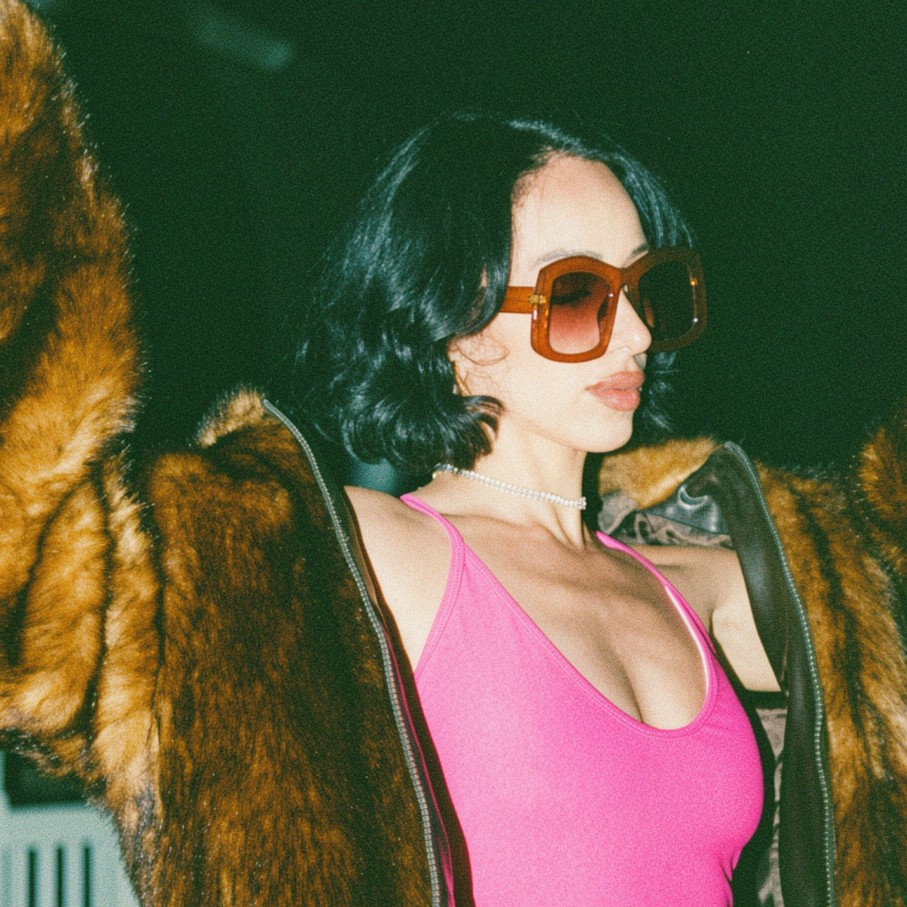 Person wearing a bright pink swimsuit with a fur coat and sunglasses indoors.