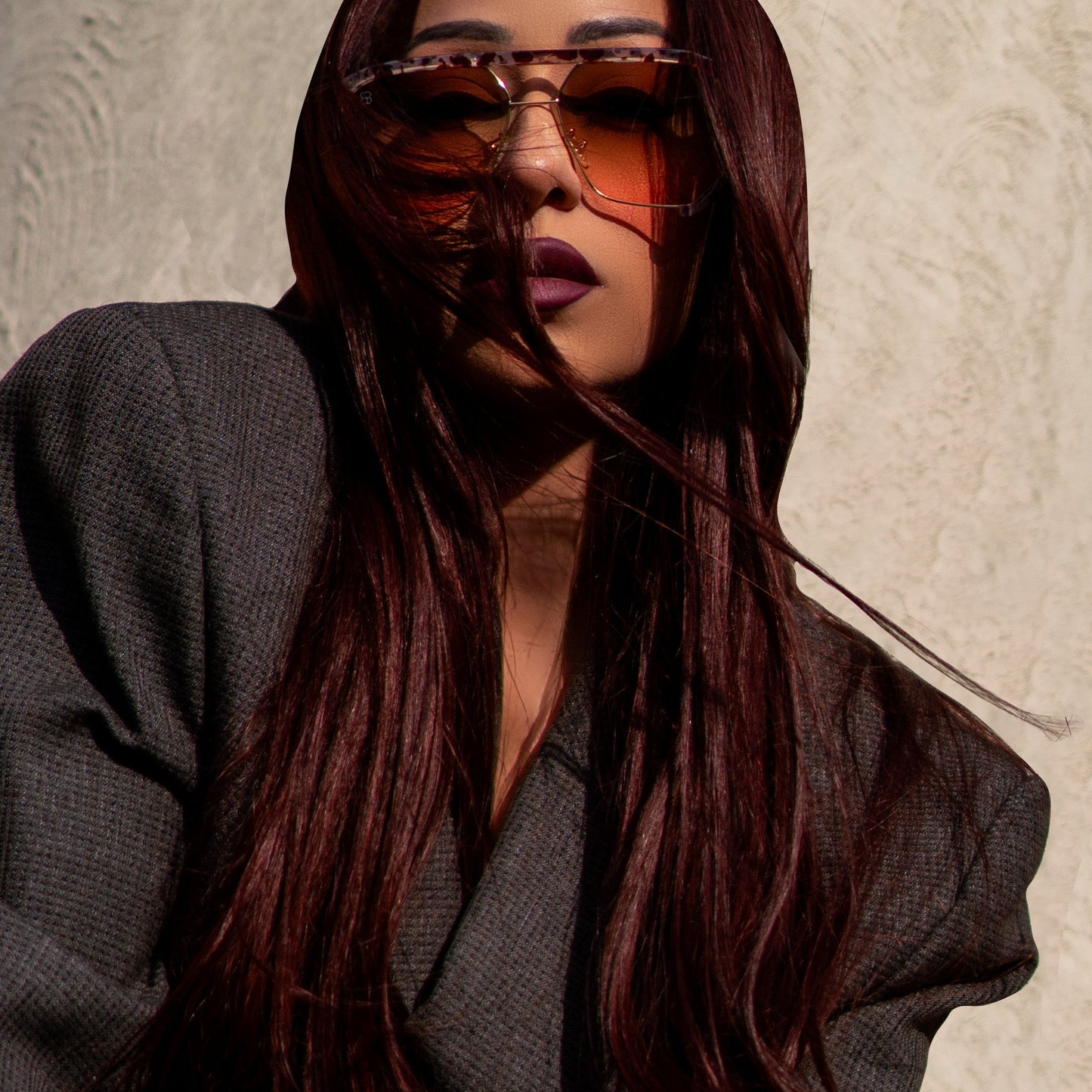 Marissa Roche wearing 1980nine sunglasses and a dark outfit against a neutral background with long red hair