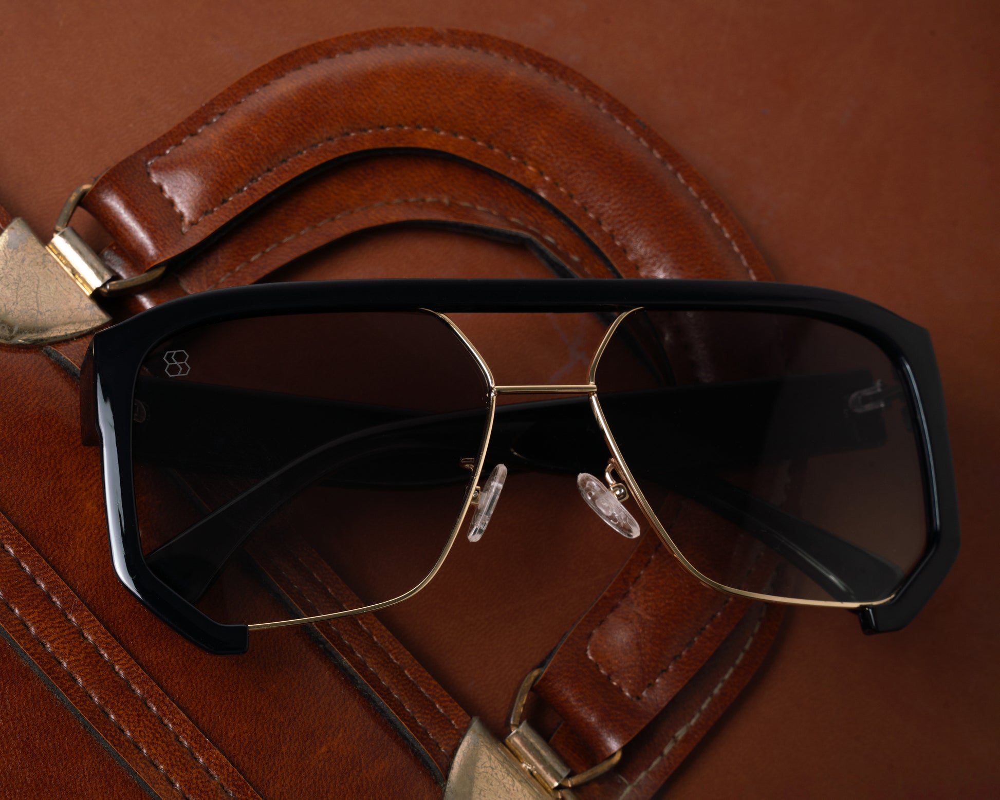 1980nine sunglasses with black and gold frame on a brown leather surface