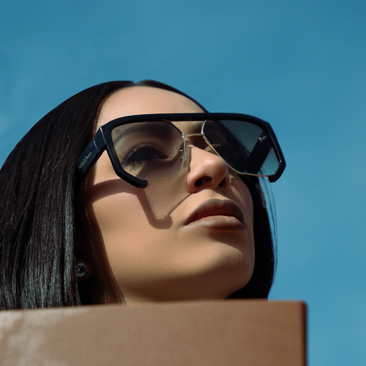 Woman wearing 1980nine sunglasses holding notebook with blue sky behind her