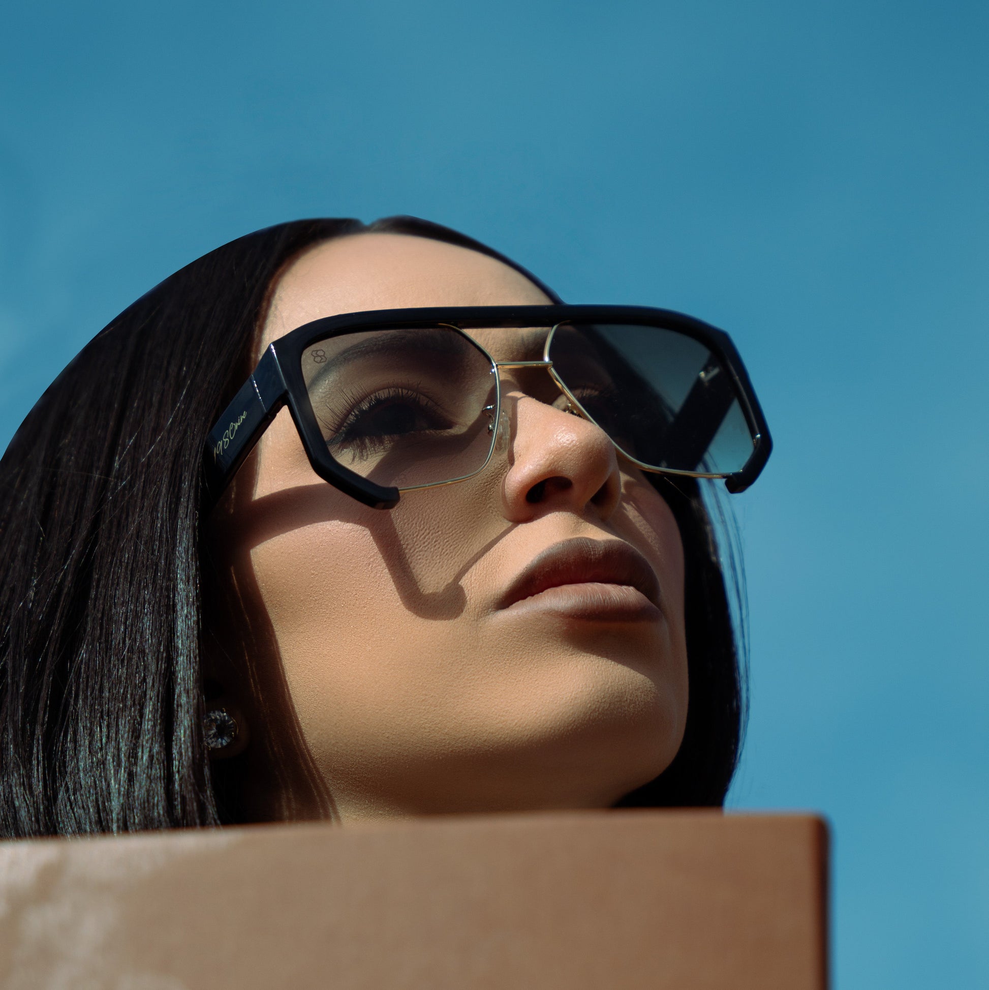 Woman wearing 1980nine sunglasses holding notebook with blue sky behind her