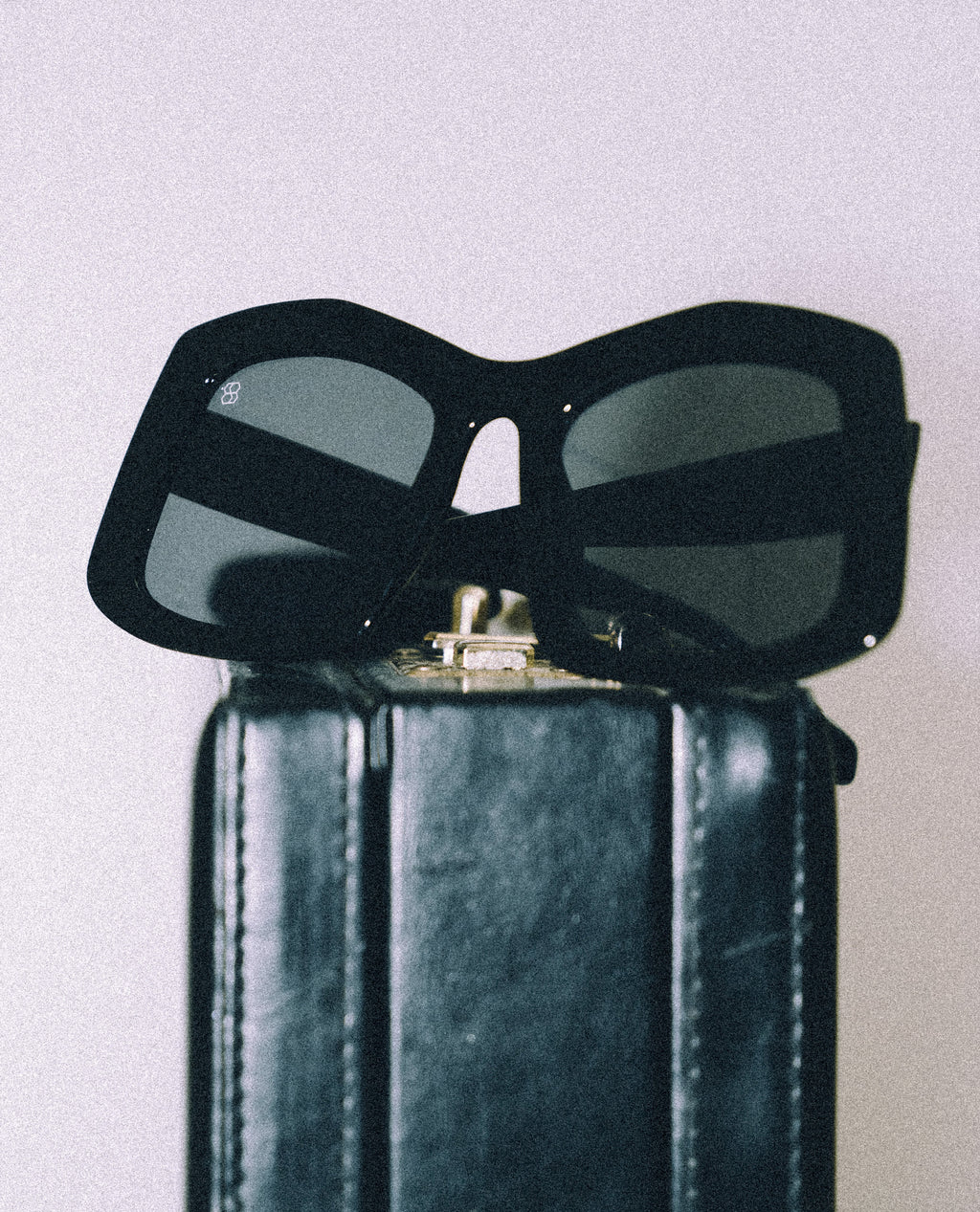 Black sunglasses on top of a black leather bag against a light gray background