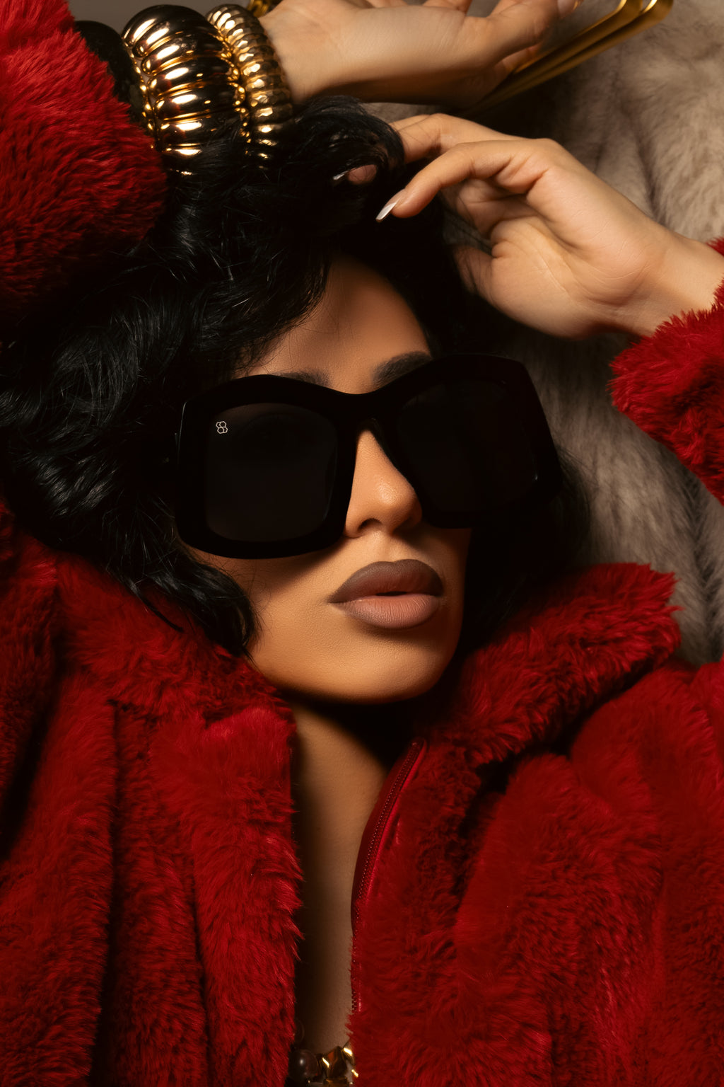 woman wearing a red fur coat and black sunglasses with a gold headpiece.