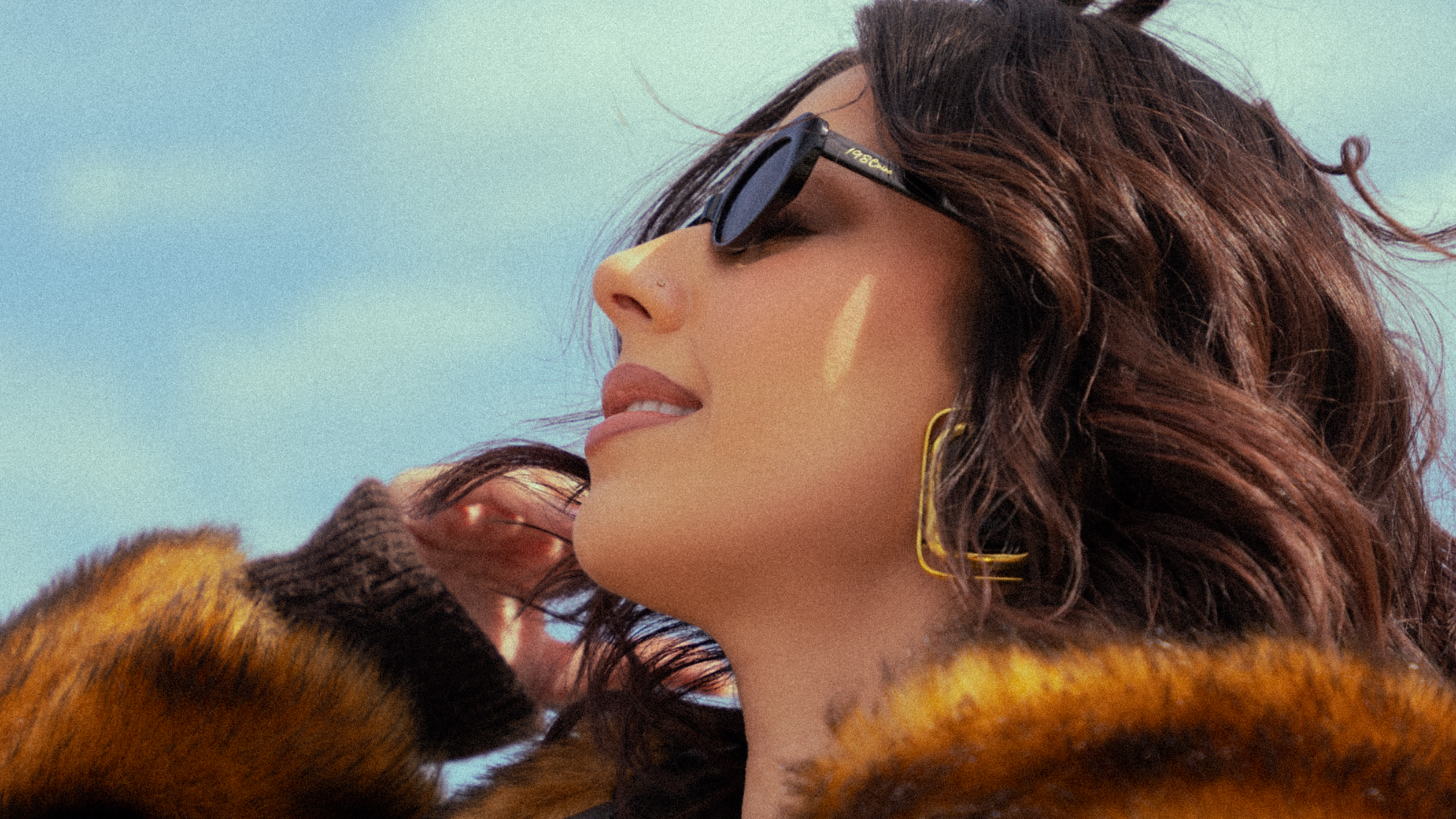 Woman wearing a fur coat and sunglasses against a blue sky.