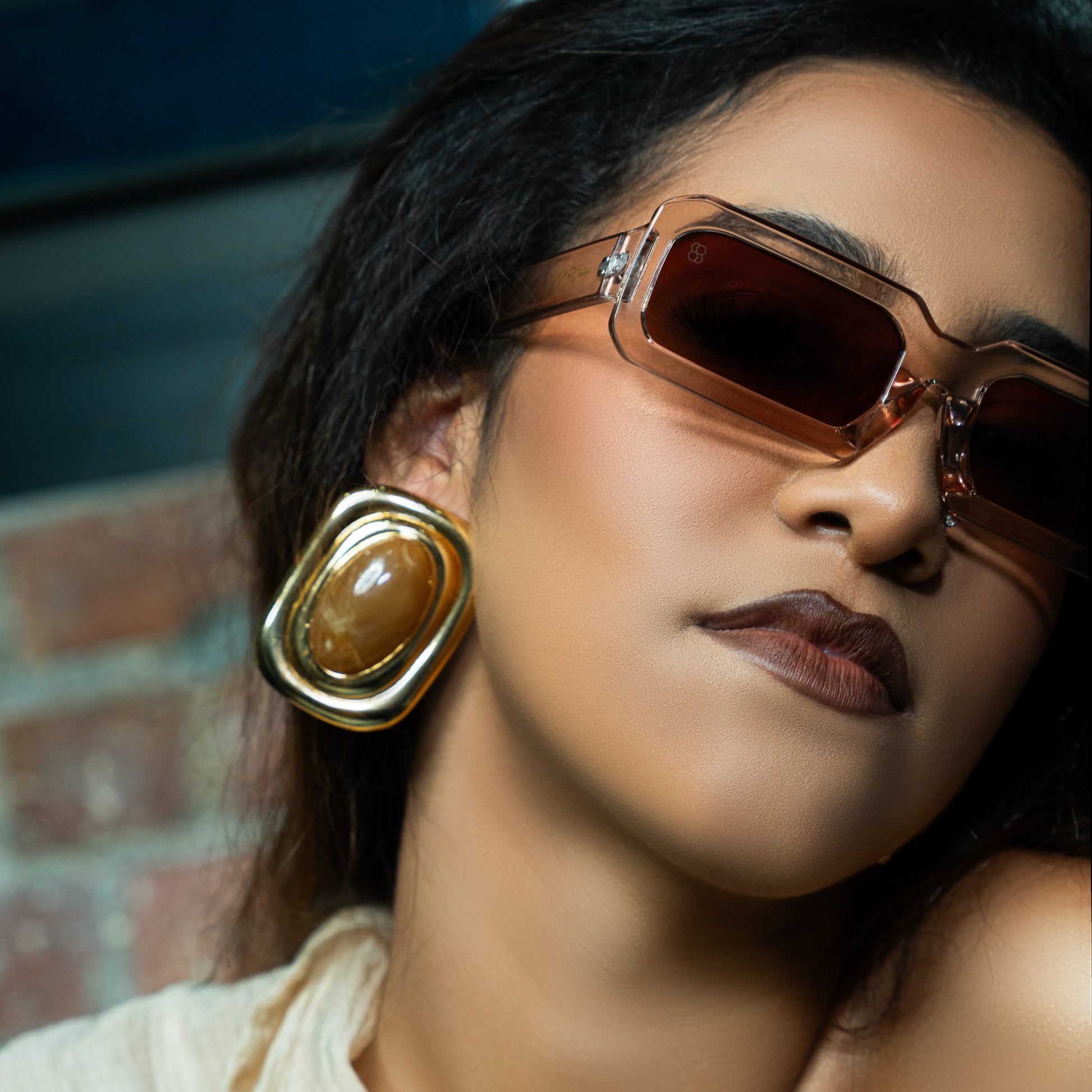 Woman wearing sunglasses and gold earrings with a blurred background