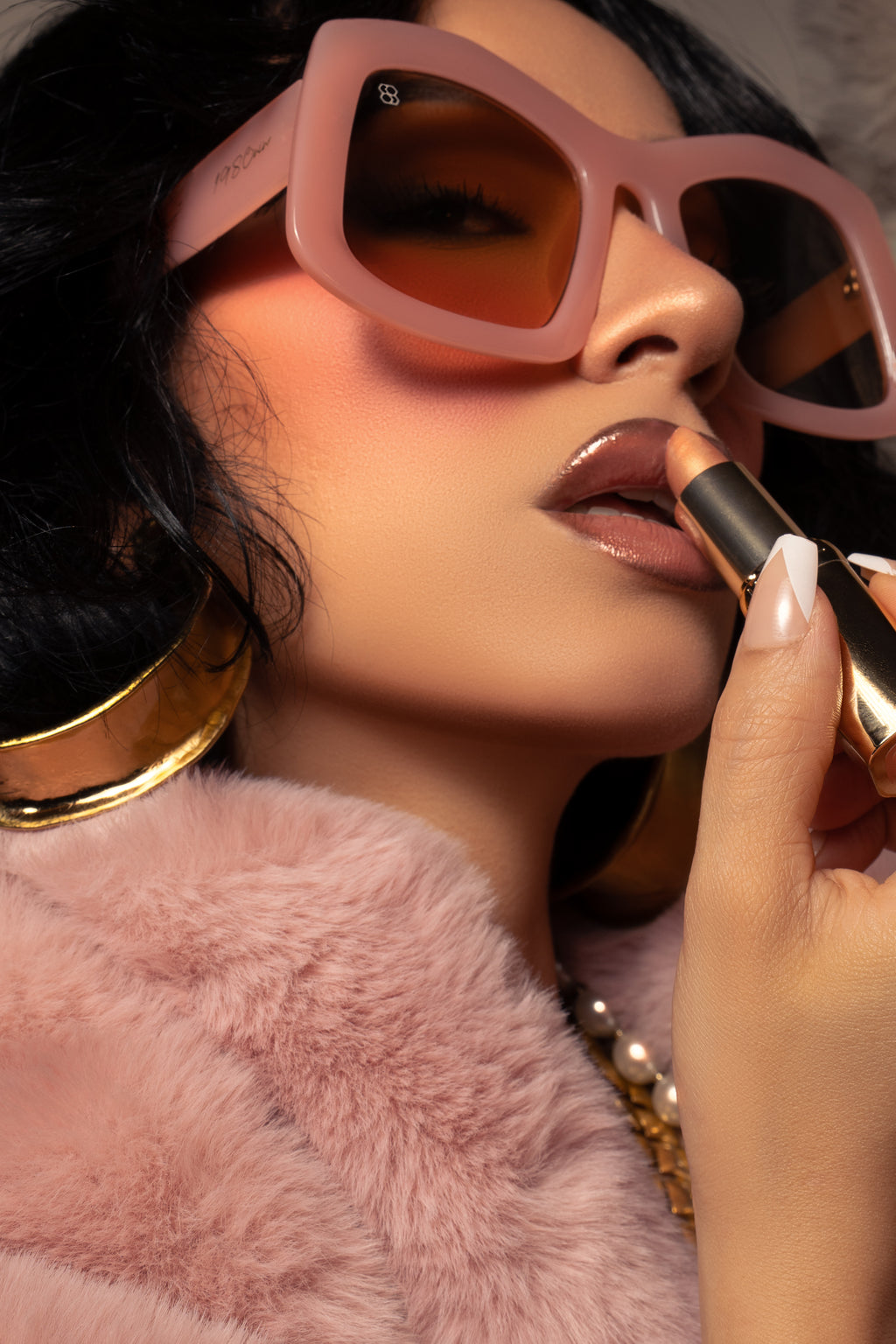 Woman applying lipstick with pink sunglasses and a fluffy pink jacket