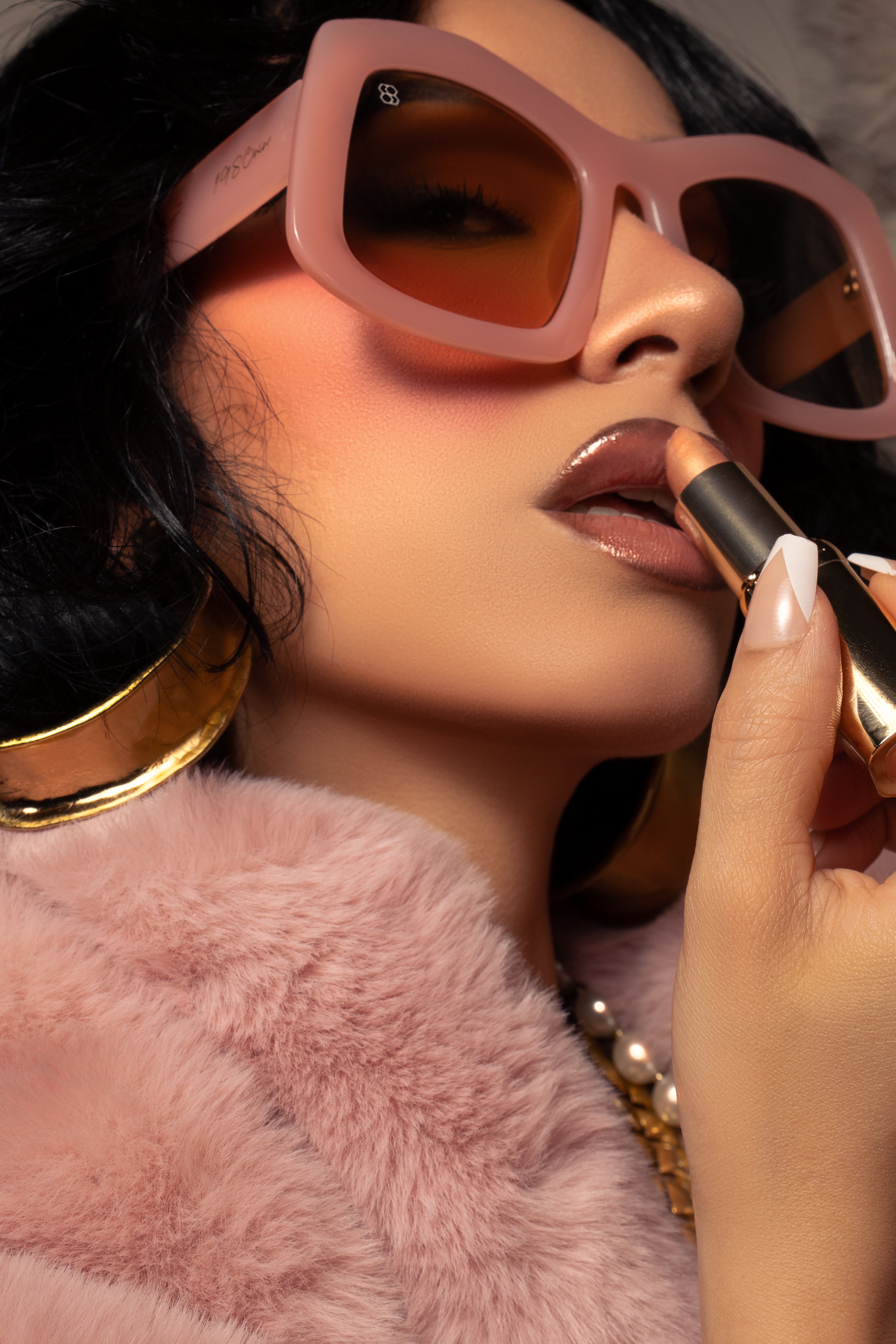 Woman applying lipstick with pink sunglasses and a fluffy pink jacket