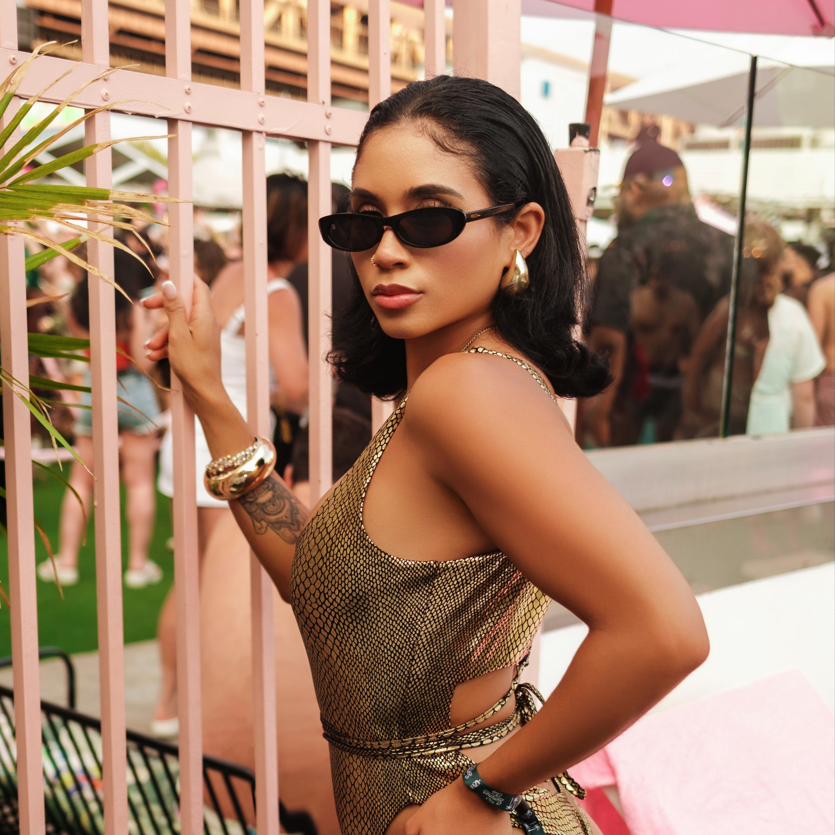 Woman in a gold chainmail outfit posing in a social setting with blurred people in the background