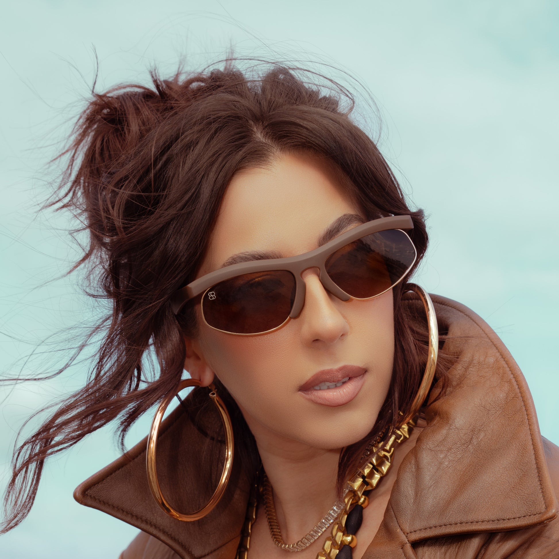 Woman wearing 1980nine sunglasses and a brown coat with a blurred background