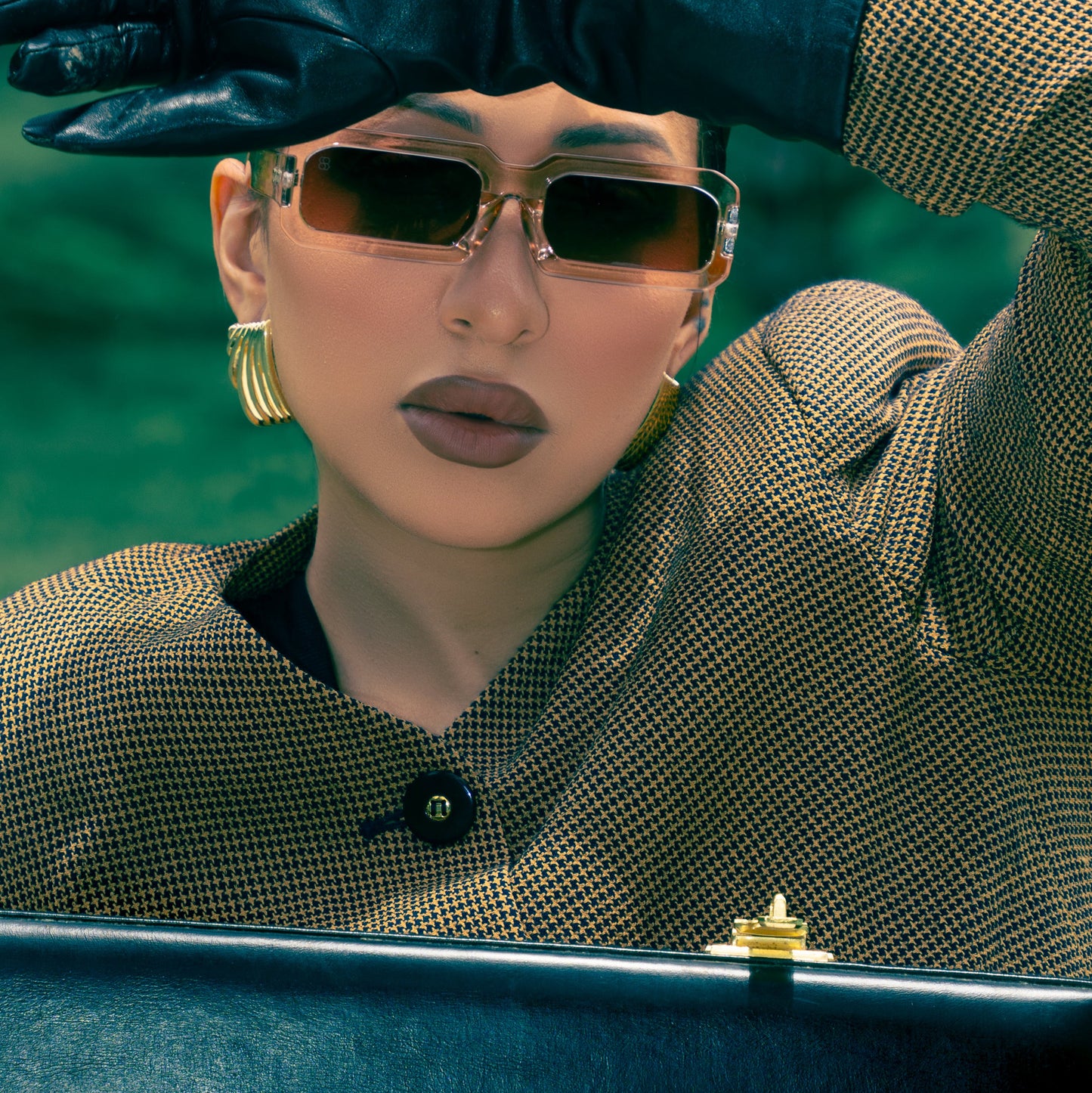 Person wearing sunglasses, gloves, and a patterned coat with a blurred background