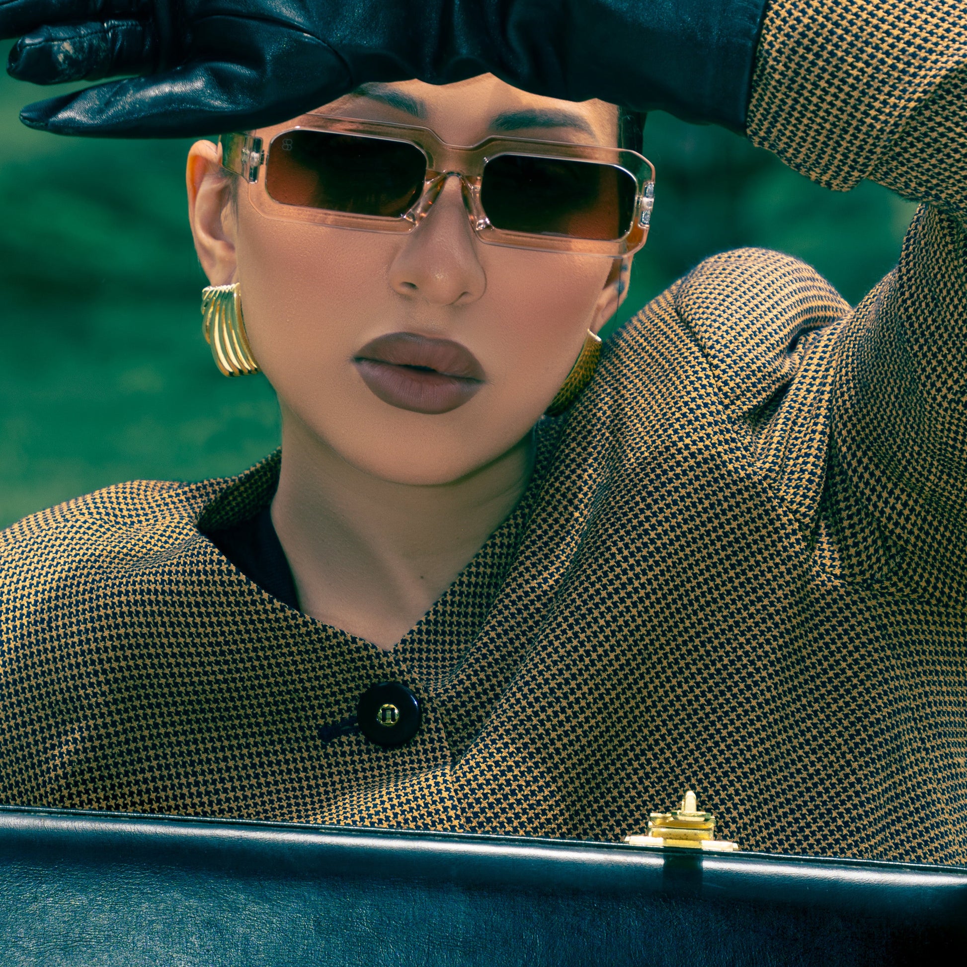 Person wearing sunglasses, gloves, and a patterned coat with a blurred background