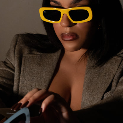 Model wearing bold yellow rectangular sunglasses with thick sculpted rims and dark tinted lenses.